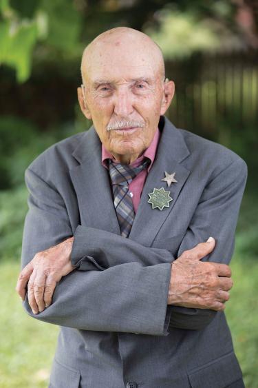 Vertical portrait of Ed Bearss standing outside in a sport coat and medals, with his arms crossed
