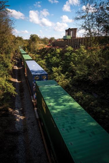 Train passing through a closely wooded path, with construction to fix erosion visible in upper right