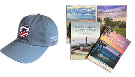 Various magazine covers stacked on top of one another, a baseball hat with an American Battlefield Trust logo and a man wearing a hoodie with an American Battlefield Trust logo design on it.
