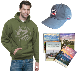 Various magazine covers stacked on top of one another, a baseball hat with an American Battlefield Trust logo and a man wearing a hoodie with an American Battlefield Trust logo design on it.